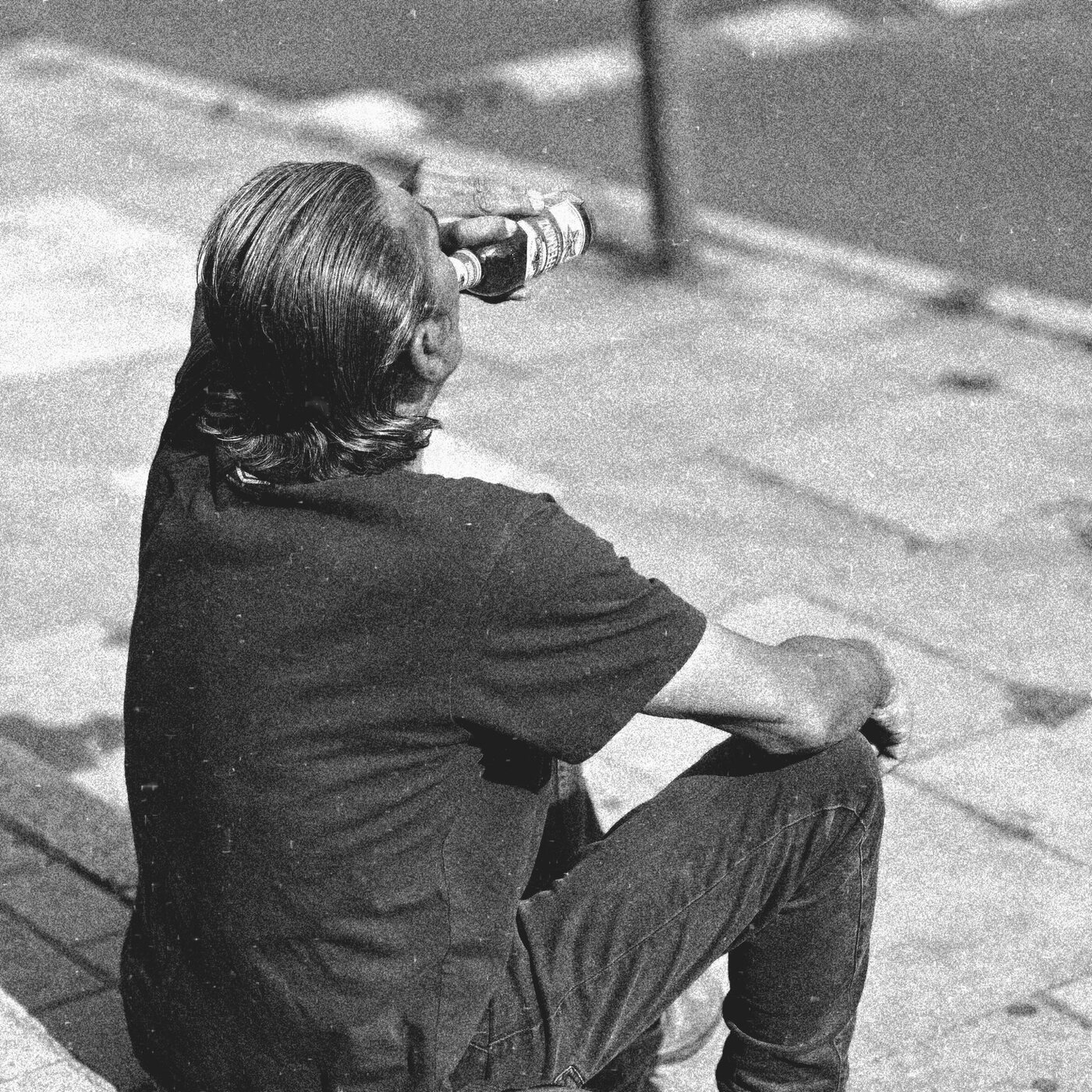 A solitary seated figure drinking in an urban space