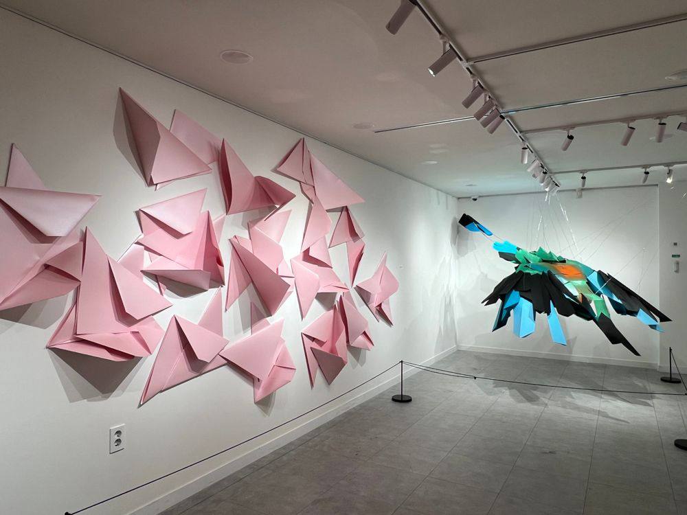Suspended sculptural bird installation with folded paper wall piece